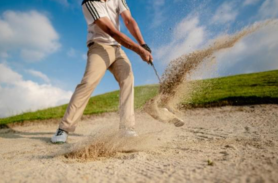 A golfer holding a full follow-through after a bunker shot