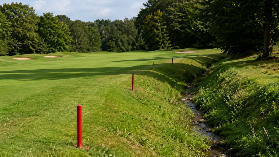 Red stakes marking a lateral penalty area beside a fairway